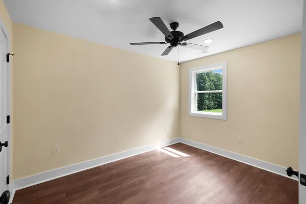 an empty room with wooden floor ceiling fan and windows
