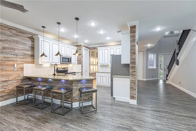 a kitchen with stainless steel appliances kitchen island granite countertop a refrigerator a stove a oven and white cabinets with wooden floor