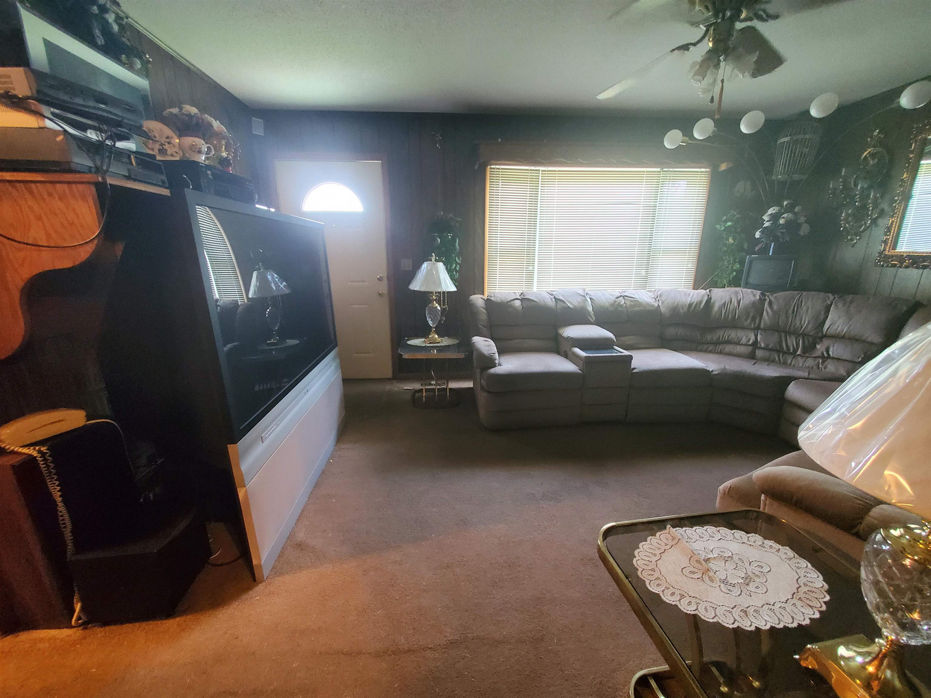 147 Rogers Street Sharon, TN 38255 - Photo 7 of 16 Carpeted living area featuring paneling walls, a front entry door with an arched window, and a ceiling fan with light fixtures