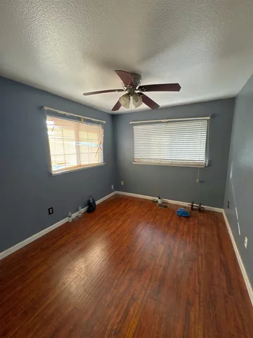 an empty room with wooden floor chandelier fan and windows