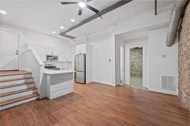 a living room with stainless steel appliances kitchen island hardwood floor and a ceiling fan