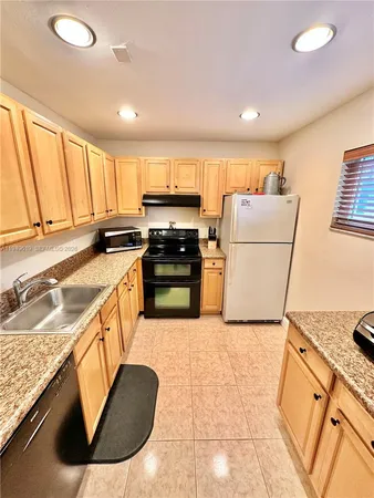 a kitchen with kitchen island granite countertop a sink a stove top oven a refrigerator a counter top space and cabinets