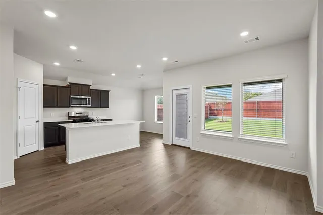 a kitchen with stainless steel appliances granite countertop a stove top oven a sink dishwasher a refrigerator and a microwave oven with wooden floor