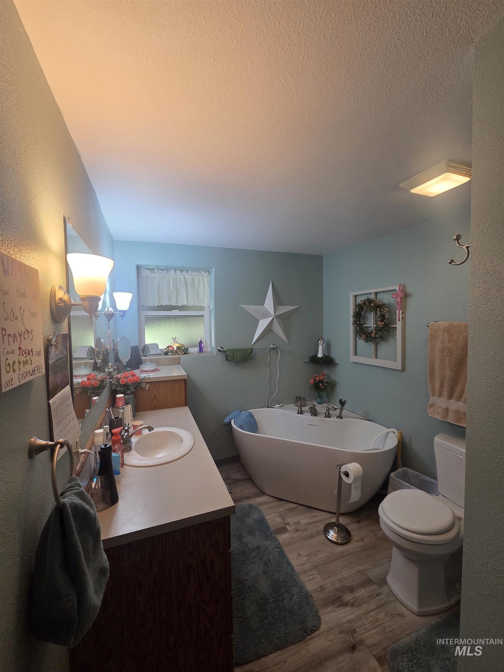 109 South 3rd Street Pomeroy, WA 99347 - Photo 17 of 36 Bathroom featuring a freestanding soaking tub, wood-finish flooring, a single vanity with an integrated sink, and a window with privacy curtains