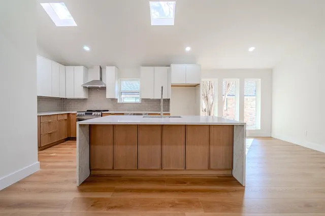 a large white kitchen with wooden floor and a window
