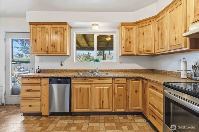 a kitchen with granite countertop a sink cabinets stainless steel appliances and a window