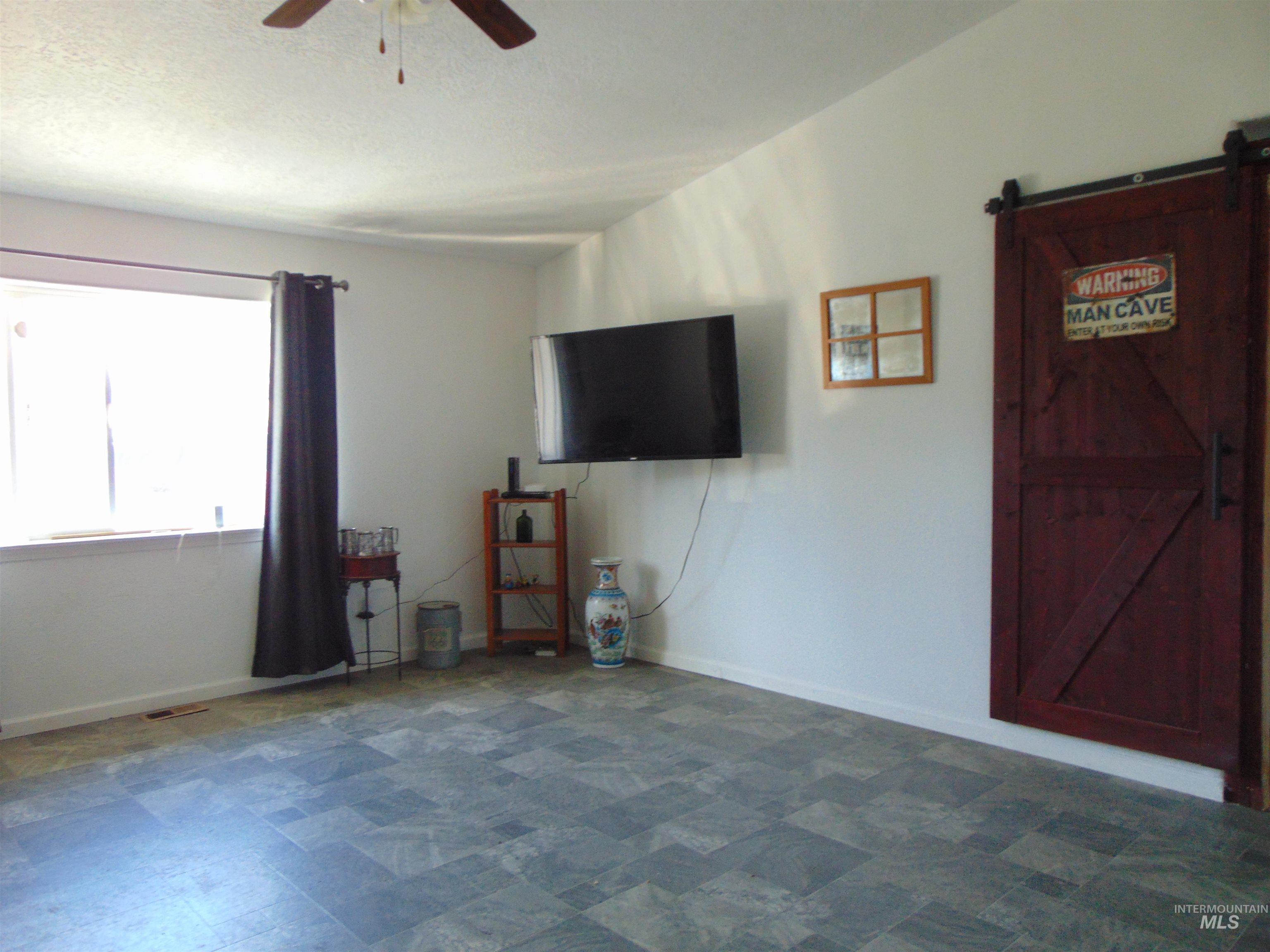 30 Maple Drive Weiser, ID 83672 - Photo 2 of 17 Unfurnished living room with a barn door, dark flooring, and ceiling fan