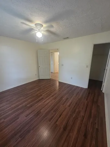 a view of an empty room with wooden floor and a ceiling fan