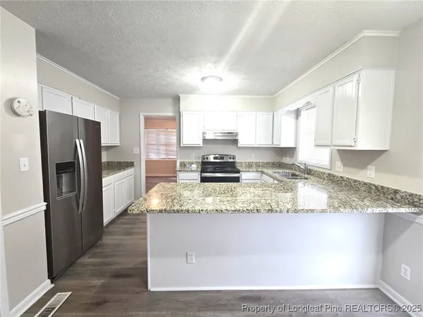 a large kitchen with granite countertop a refrigerator a stove a sink a stove a oven with white cabinets