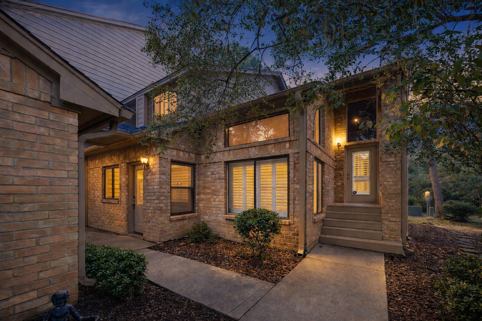 12 Lakeridge Drive Spring, TX 77381 - Photo 2 of 24 Curb appeal at its finest: Warm exterior lighting highlights the classic brick architecture, clean rooflines, and mature trees of this private, tucked-away home.