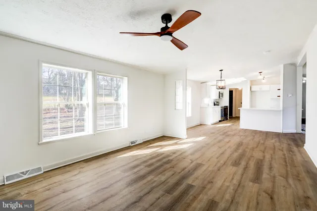 an empty room with wooden floor ceiling fan and windows