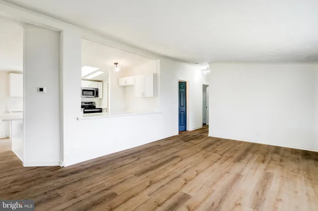 a view of an empty room with wooden floor and a kitchen