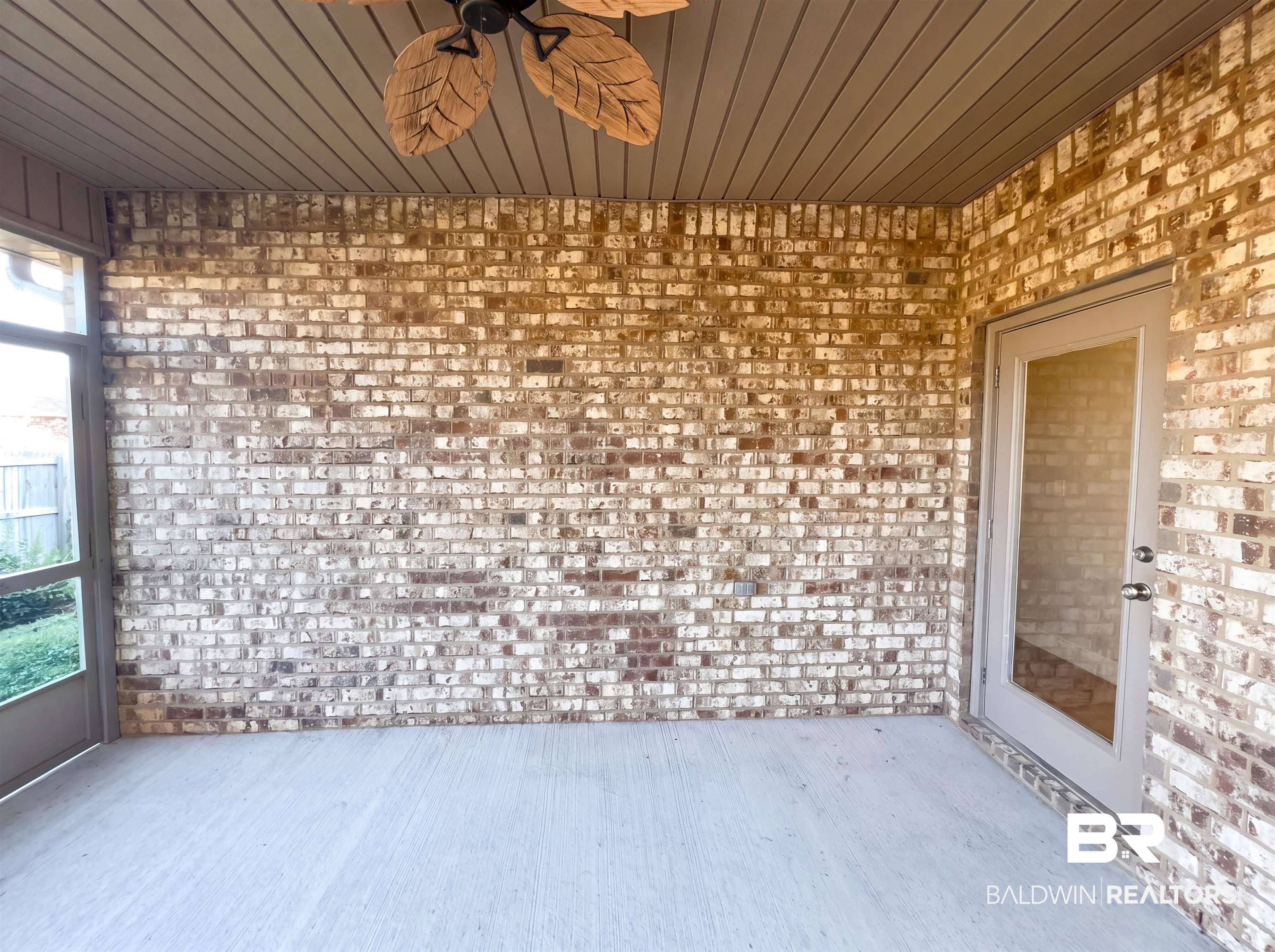 1740 Covington Lane Foley, AL 36535 - Photo 17 of 18 Screened patio featuring a solid brick wall, concrete flooring, a ceiling fan with leaf-shaped blades, and a white glass-paneled door