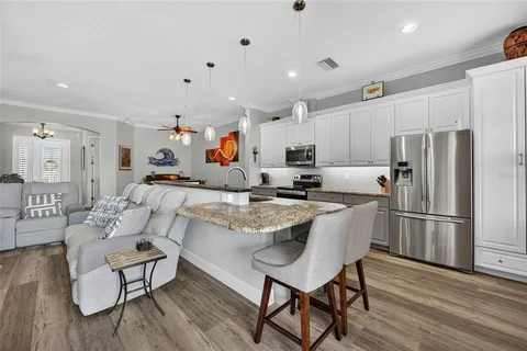 a kitchen with stainless steel appliances granite countertop a refrigerator a sink dishwasher a dining table and chairs with wooden floor