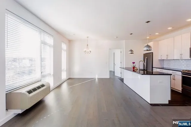 a large kitchen with kitchen island granite countertop a stove a sink a refrigerator and white cabinets with wooden floor