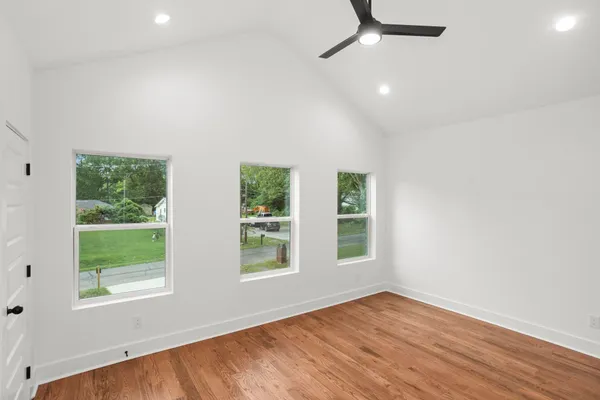 an empty room with wooden floor ceiling fan and windows