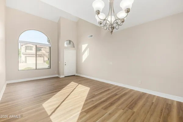 an empty room with wooden floor chandelier and windows