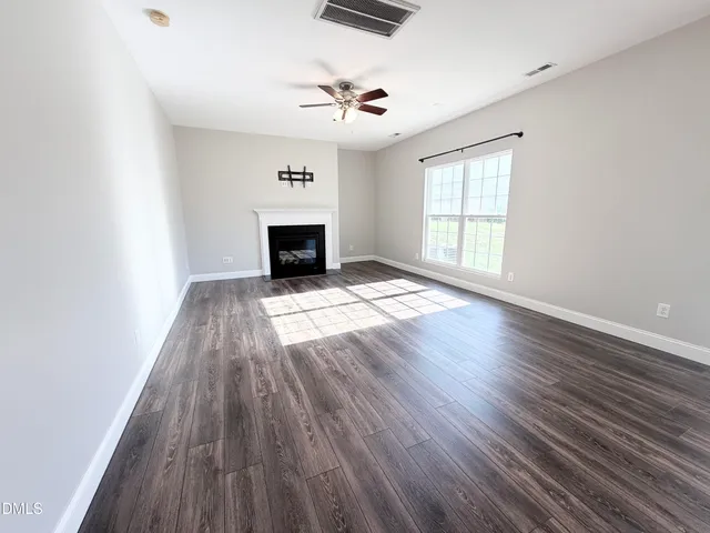 an empty room with wooden floor fireplace and windows