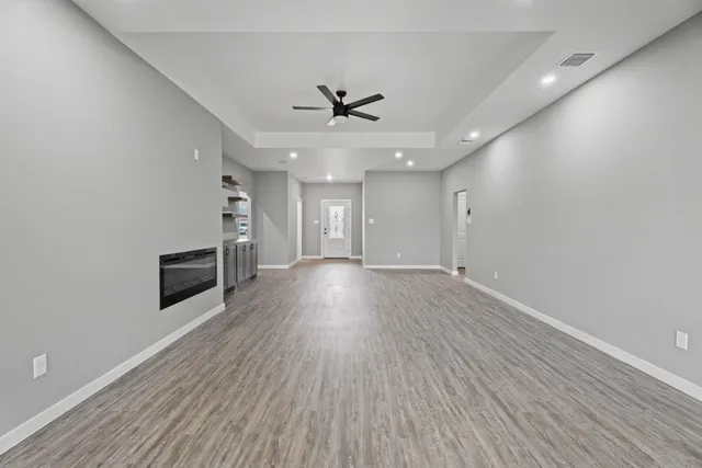 an empty room with wooden floor ceiling fan and windows