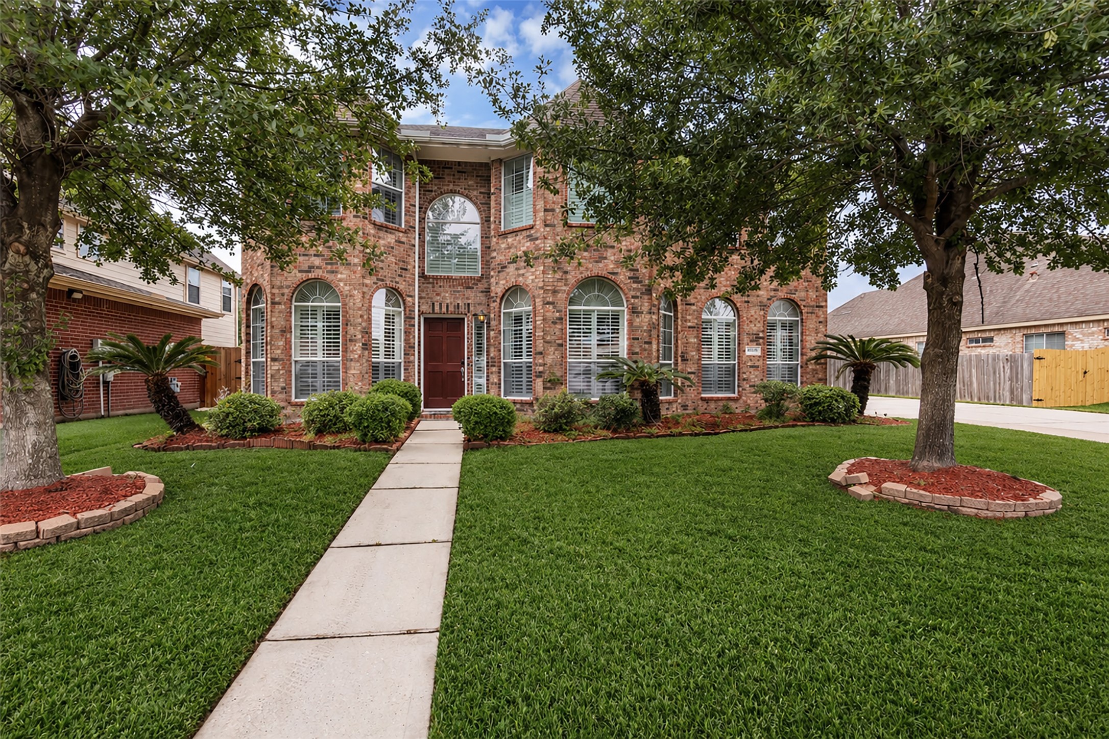 6807 Chapelfield Lane Houston, TX 77049 - Photo 2 of 42 This is a two-story brick home with large arched windows and a well-maintained front lawn. Flanked by trees and landscaped with shrubs, it features a welcoming walkway leading to the entrance.