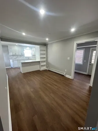 an empty room with wooden floor and kitchen view
