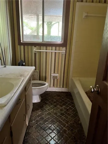 a bathroom with a granite countertop sink a toilet a window and tub