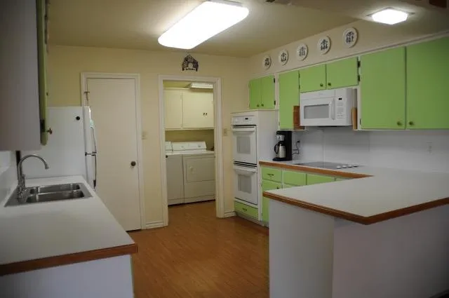 a kitchen with green cabinets a sink and dishwasher a refrigerator with wooden floor