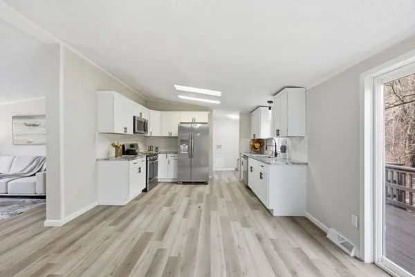 a large white kitchen with kitchen island a sink dishwasher stove and white cabinets with wooden floor