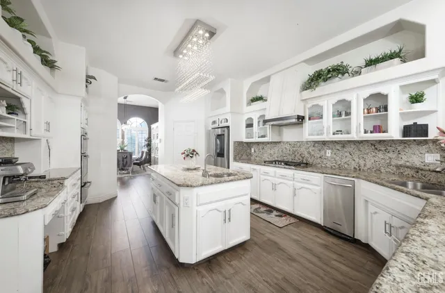 a large white kitchen with stainless steel appliances granite countertop a lot of counter space and wooden floors