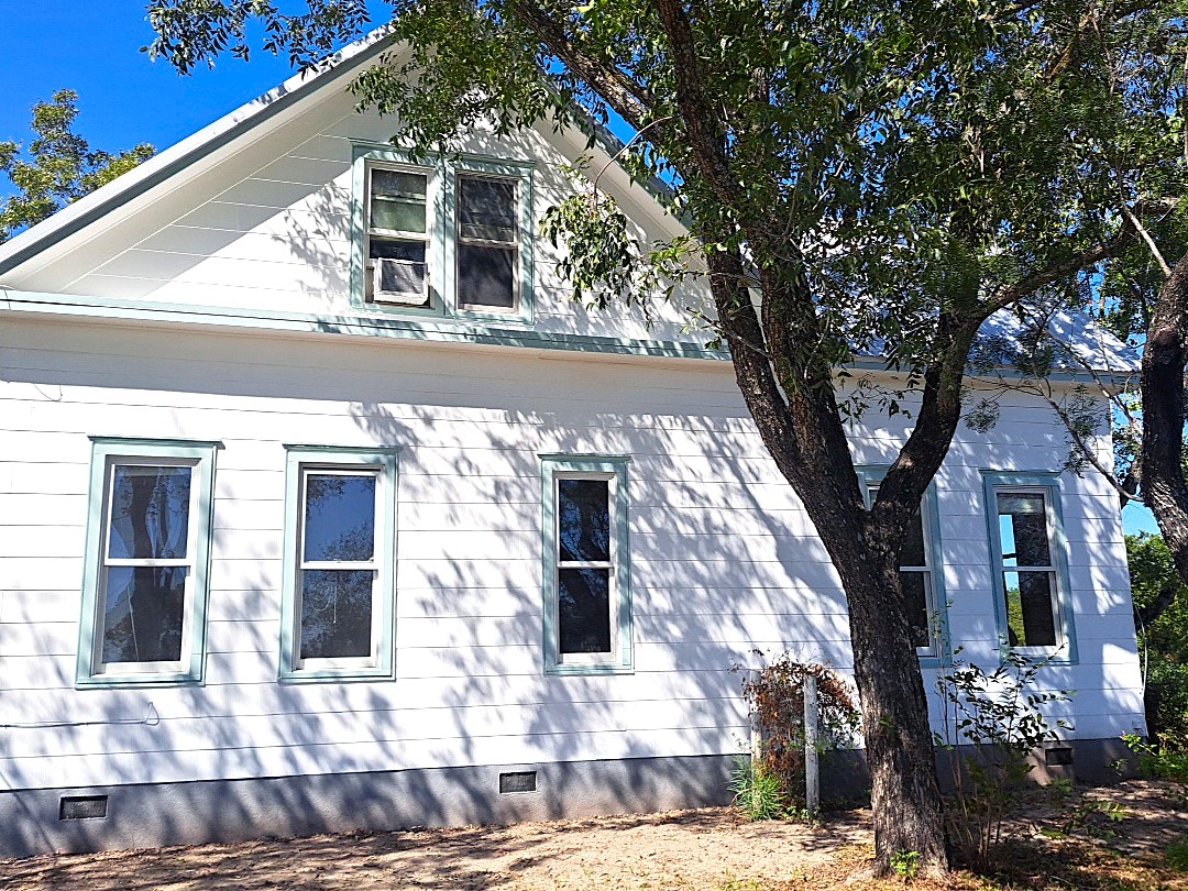 Mature trees shade a classic siding exterior featuring multi-pane windows and a raised foundation.