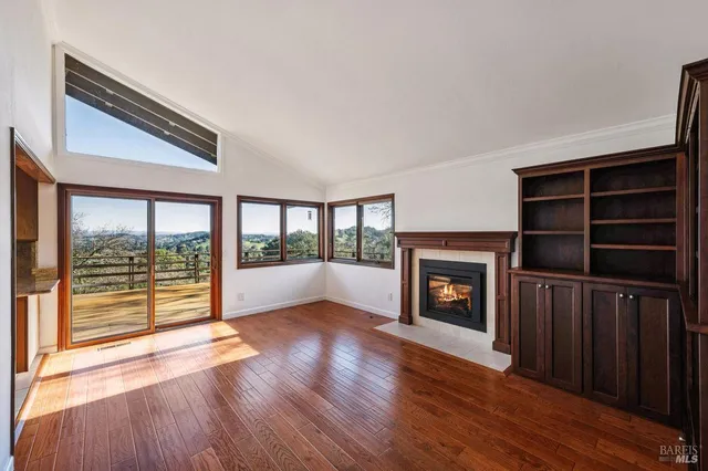 a view of an empty room with wooden floor fireplace and a window
