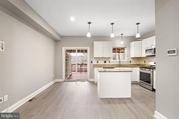 a kitchen with granite countertop a stove a sink dishwasher a refrigerator and white cabinets with wooden floor