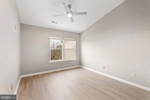 an empty room with wooden floor ceiling fan and windows