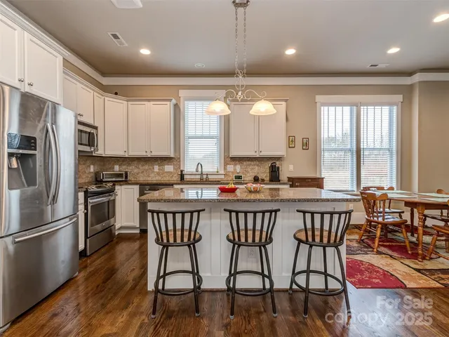 a kitchen with stainless steel appliances granite countertop a table chairs a sink dishwasher a refrigerator and microwave