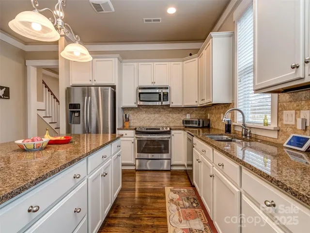 a large kitchen with granite countertop a lot of white cabinets and stainless steel appliances