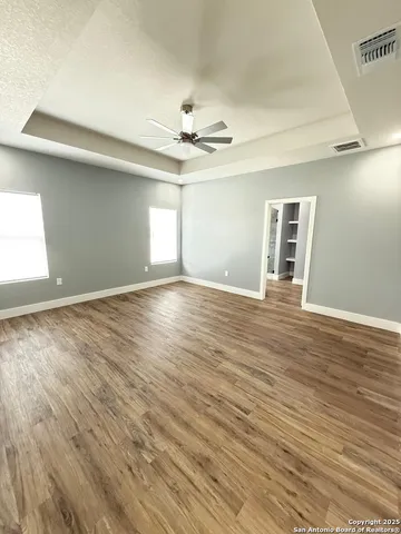 an empty room with wooden floor chandelier fan and windows