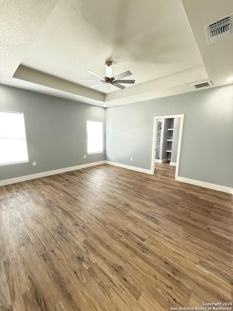 802 Cr 520 D'Hanis, TX 78850 - Photo 11 of 16 an empty room with wooden floor chandelier fan and windows