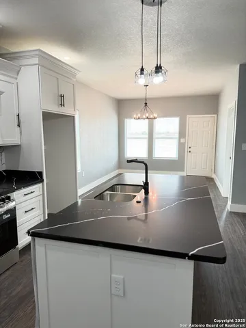 a kitchen with kitchen island a stove a sink and white cabinets with wooden floor