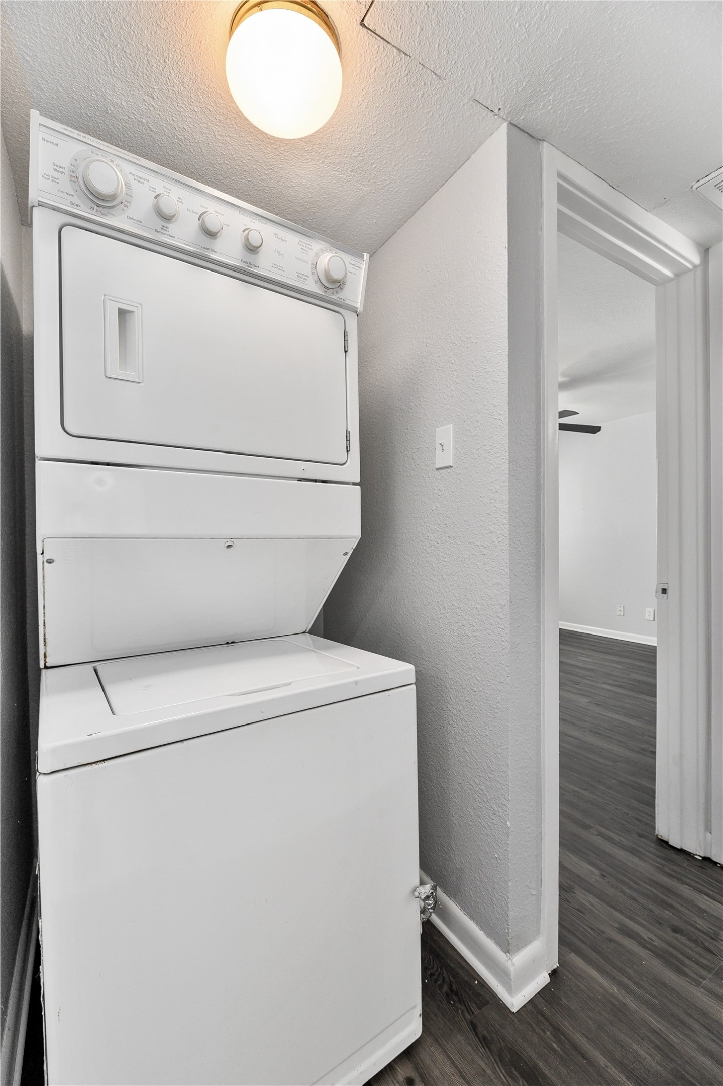 2408 Longview Street, Unit 113 Austin, TX 78705 - Photo 21 of 23 Laundry room featuring a textured wall, a textured ceiling, dark wood-type flooring, and stacked washer and clothes dryer