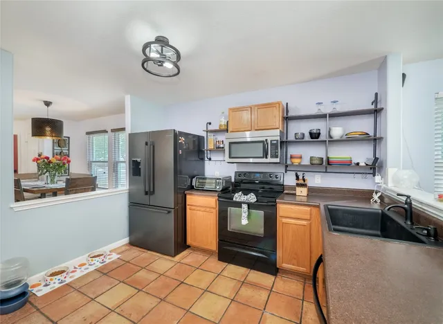 a kitchen with stainless steel appliances granite countertop a refrigerator a stove top oven a sink a dining table and chairs with wooden floor