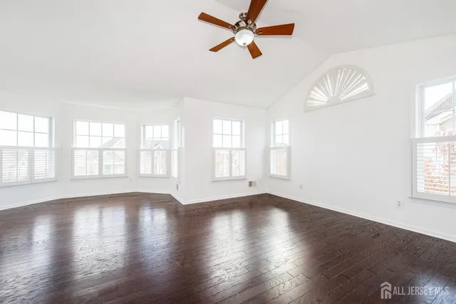 an empty room with wooden floor ceiling fan and windows