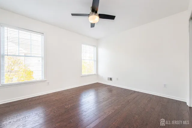 an empty room with wooden floor chandelier fan and windows