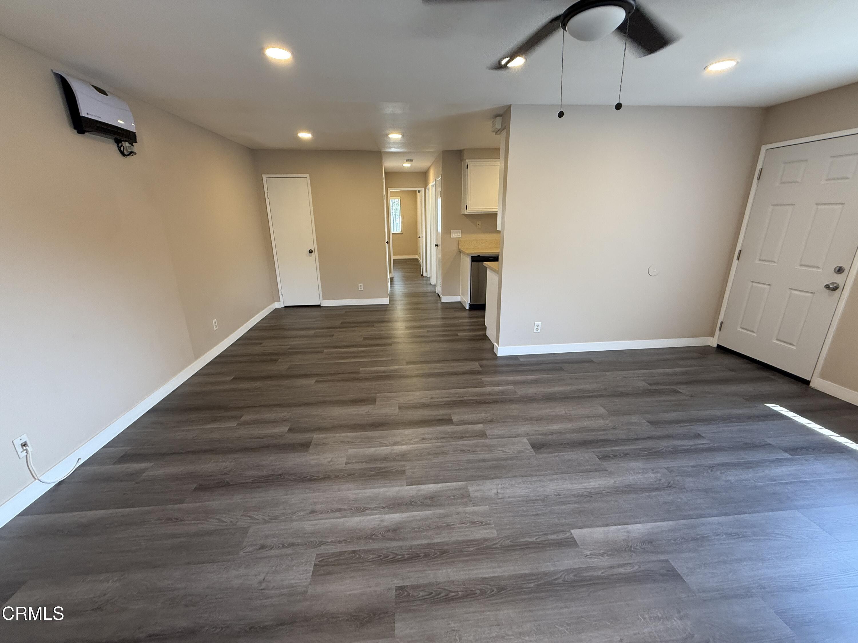 an empty room with wooden floor ceiling fan and kitchen view