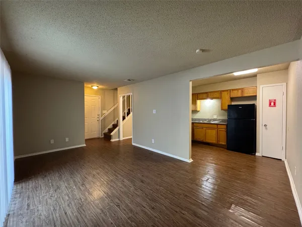 a view of empty room with wooden floor and kitchen