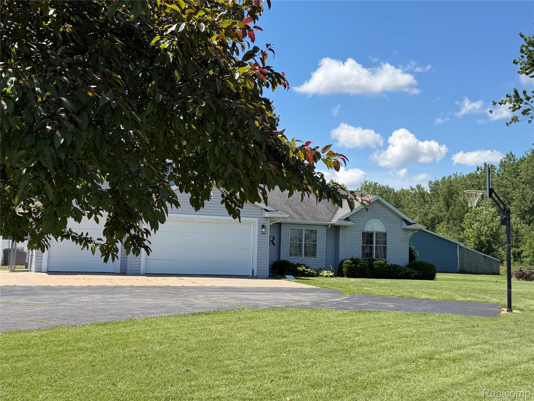 Light blue siding exterior featuring a three-car garage, arched window, and mature landscaping