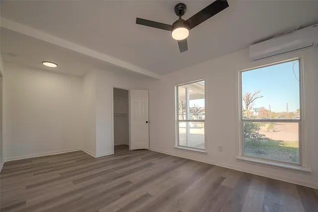 an empty room with wooden floor chandelier fan and windows