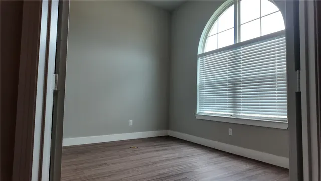 a view of an empty room with wooden floor and a window