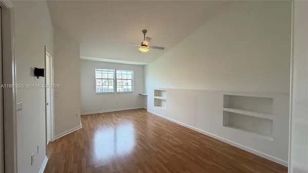 an empty room with wooden floor closet and windows