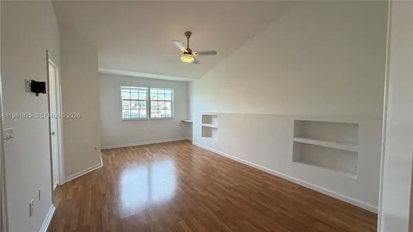 an empty room with wooden floor cabinet and windows