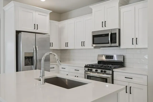 a open kitchen with stainless steel appliances granite countertop a refrigerator a sink dishwasher a stove and white cabinets with wooden floor